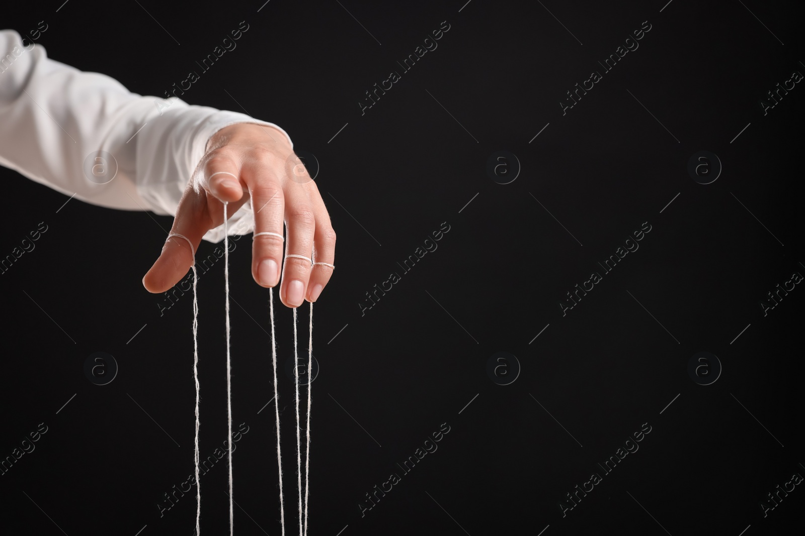 Photo of Woman pulling strings of puppet on black background, closeup. Space for text