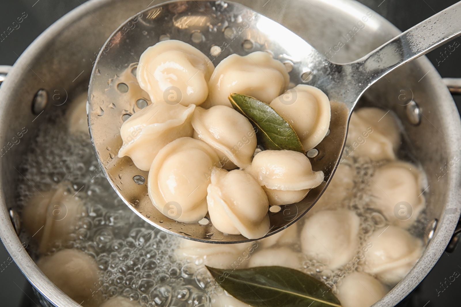 Photo of Closeup of dumplings on skimmer over stewpan with boiling water. Home cooking