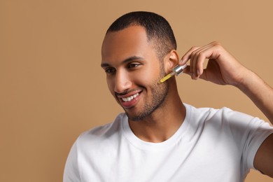 Handsome man applying cosmetic serum onto face on light brown background, space for text