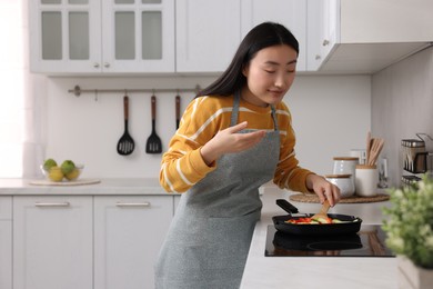 Beautiful woman cooking and smelling vegetable dish in kitchen. Space for text