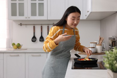 Photo of Beautiful woman cooking and smelling vegetable dish in kitchen. Space for text