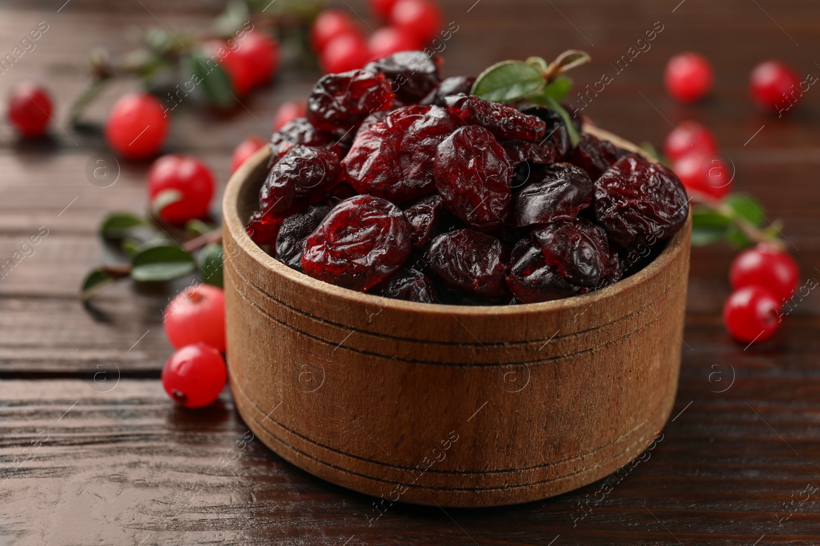 Photo of Tasty dried cranberries in bowl, fresh ones and leaves on wooden table, closeup
