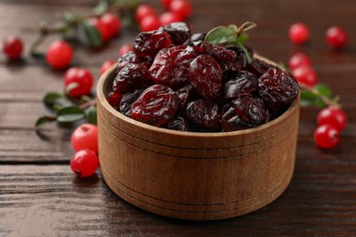 Photo of Tasty dried cranberries in bowl, fresh ones and leaves on wooden table, closeup