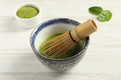 Photo of Cup of fresh matcha tea with bamboo whisk on white wooden table, closeup