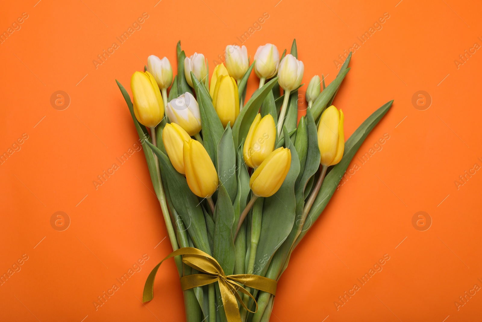 Photo of Bouquet of beautiful yellow tulips on orange background, top view