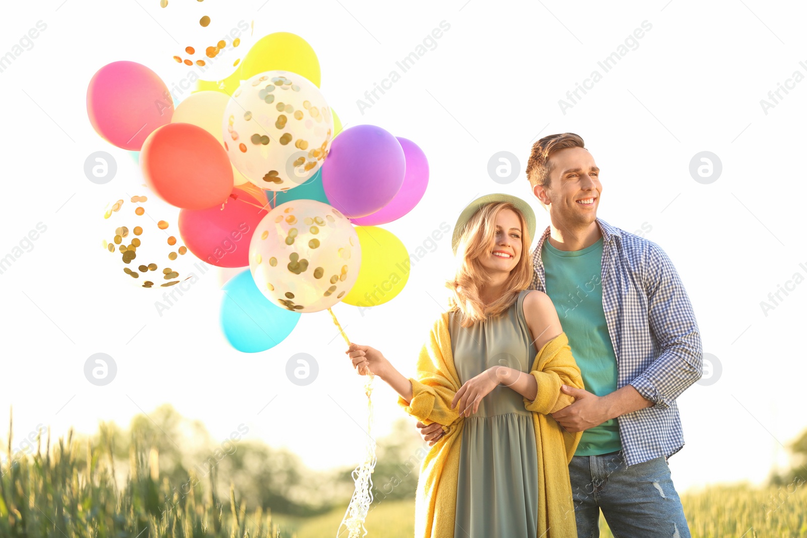 Photo of Young couple with colorful balloons in field on sunny day