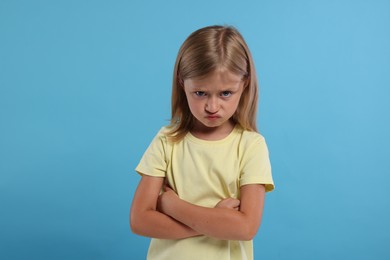 Photo of Resentment. Angry little girl with crossed arms on light blue background
