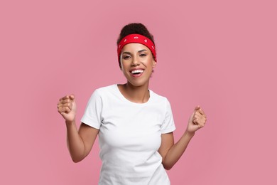 Photo of Happy young woman in stylish headband dancing on pink background