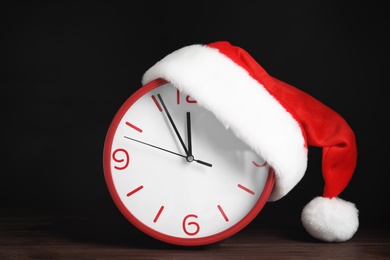 Photo of Clock with Santa hat showing five minutes until midnight on dark background. New Year countdown