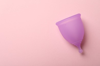 Photo of Violet menstrual cup on pink background, top view. Space for text