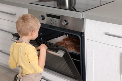 Little boy baking cookies in oven at home