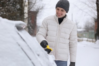 Man cleaning snow from car window outdoors