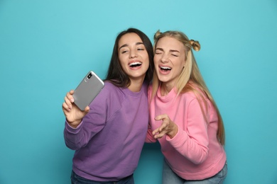 Photo of Young women laughing while taking selfie against color background