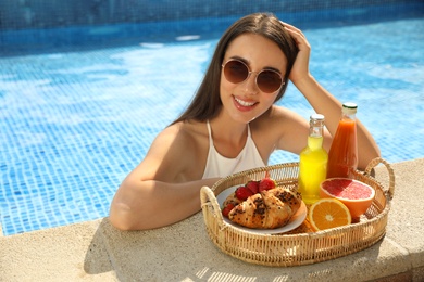 Young woman with delicious breakfast on tray in swimming pool