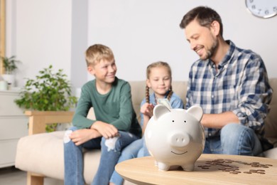 Photo of Happy family at home, focus on piggy bank. Space for text