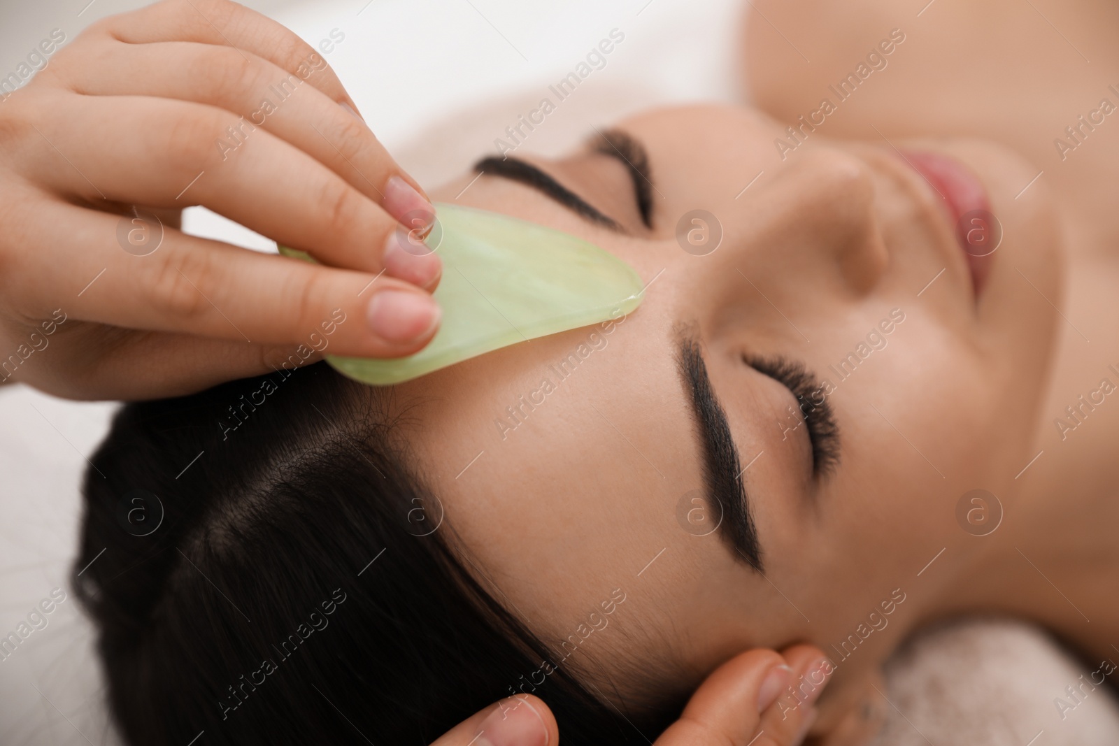 Photo of Young woman receiving facial massage with gua sha tool in beauty salon, closeup