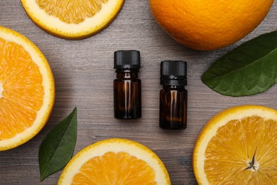 Photo of Bottles of essential oil with orange slices and leaves on wooden table, flat lay