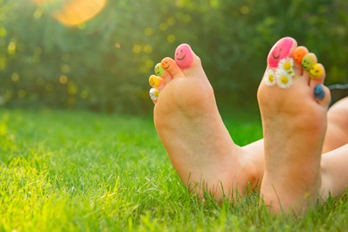 Photo of Teenage girl with chamomiles and smiling faces drawn on toes outdoors, closeup. Space for text