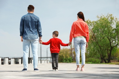Photo of Little child holding hands with his parents outdoors. Family weekend