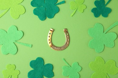 Photo of St. Patrick's day. Golden horseshoe and decorative clover leaves on green background, flat lay