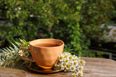 Cup of delicious chamomile tea and fresh flowers outdoors on sunny day, space for text