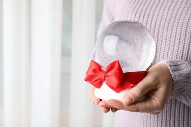 Photo of Woman holding empty snow globe with red bow indoors, closeup. Space for text