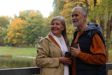 Affectionate senior couple with cups of coffee in autumn park, space for text