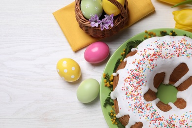 Glazed Easter cake with sprinkles, painted eggs and flowers on white wooden table, flat lay. Space for text