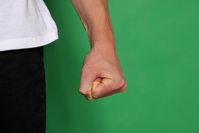 Photo of Young man showing fist on green background, closeup. Aggression concept