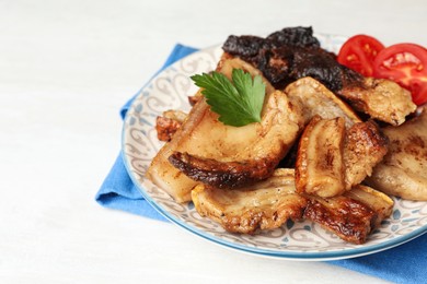 Tasty fried pork lard with parsley and tomatoes on white table, closeup