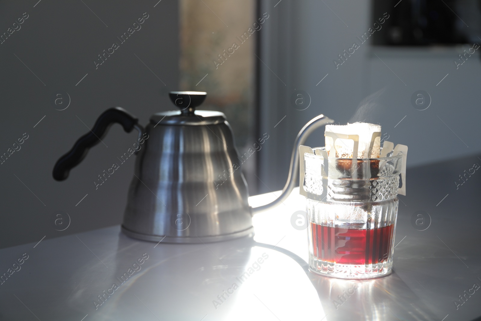Photo of Glass with drip coffee bag and kettle on light grey table