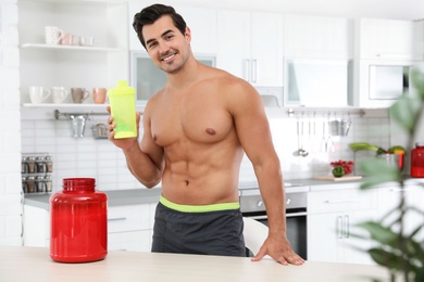 Photo of Young shirtless athletic man with protein shake powder in kitchen