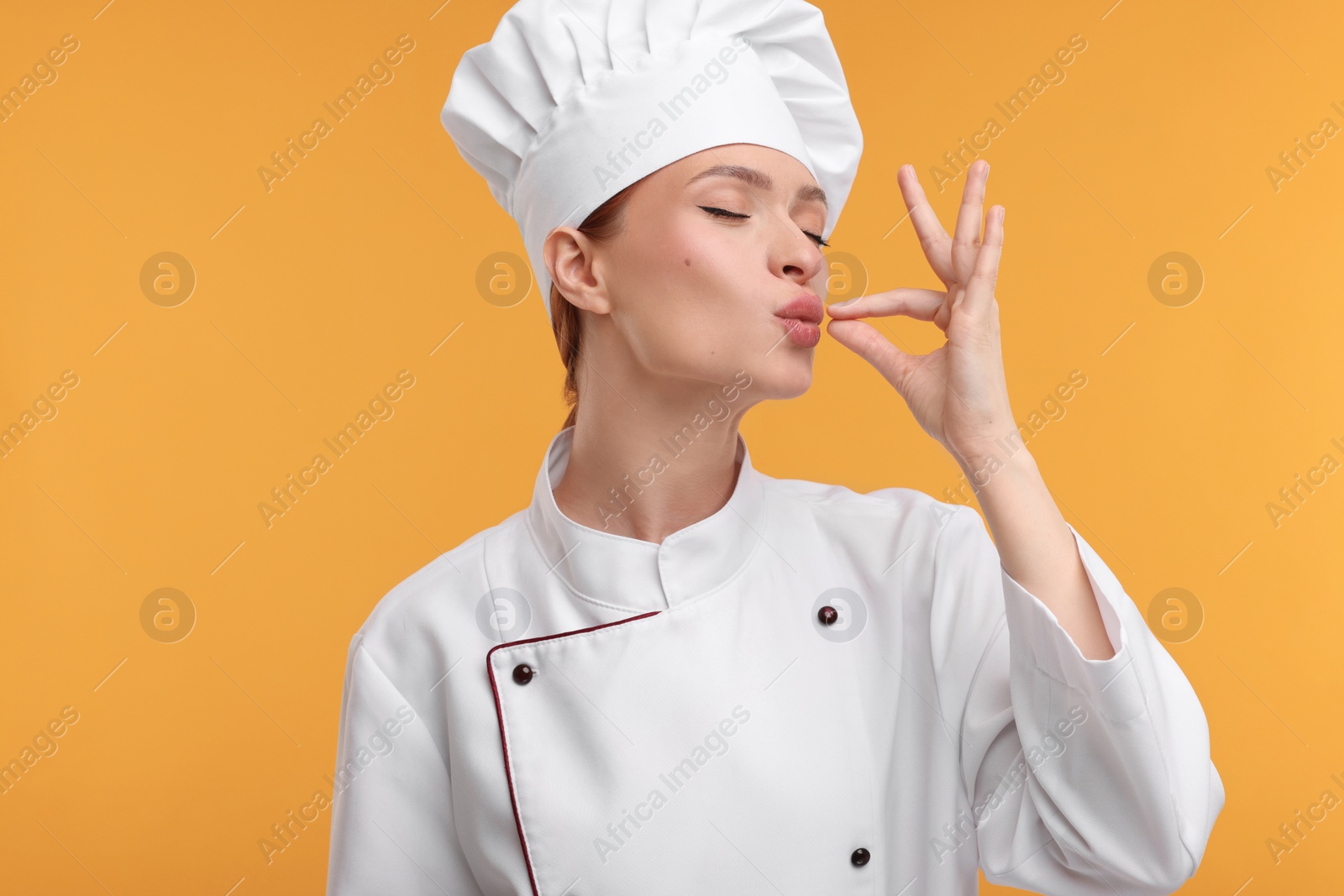 Photo of Young chef in uniform showing perfect sign on orange background