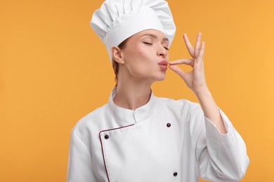 Young chef in uniform showing perfect sign on orange background