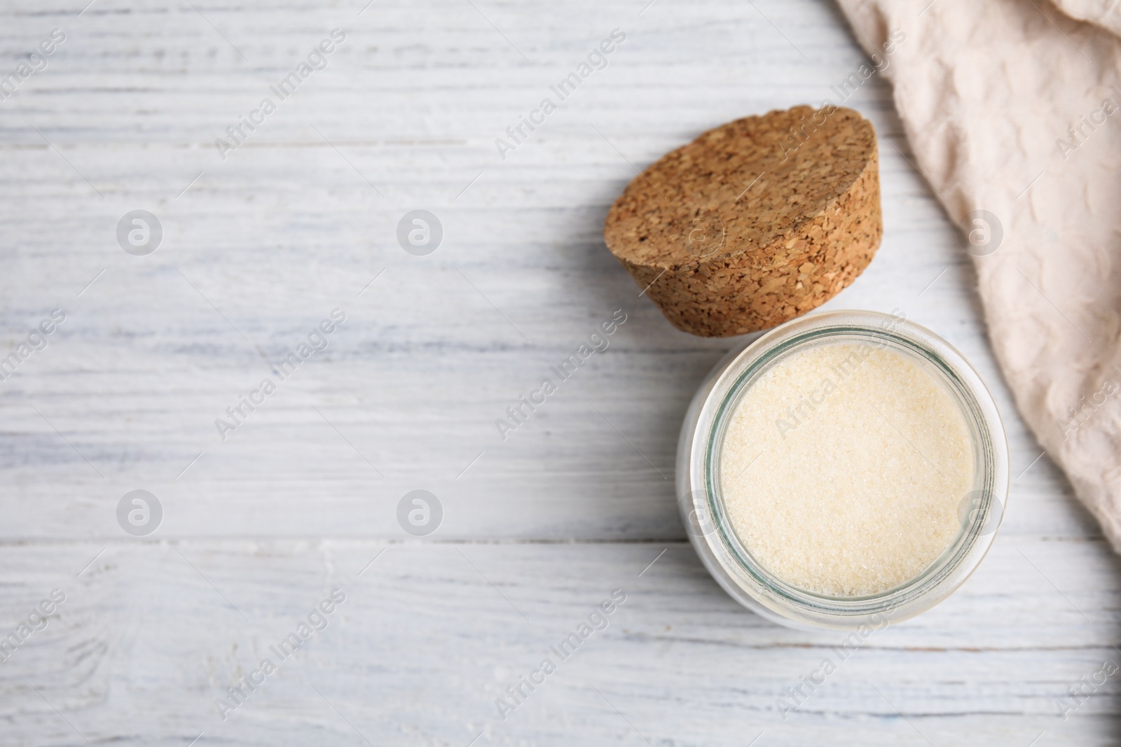 Photo of Gelatin powder in glass jar on white wooden table, flat lay. Space for text