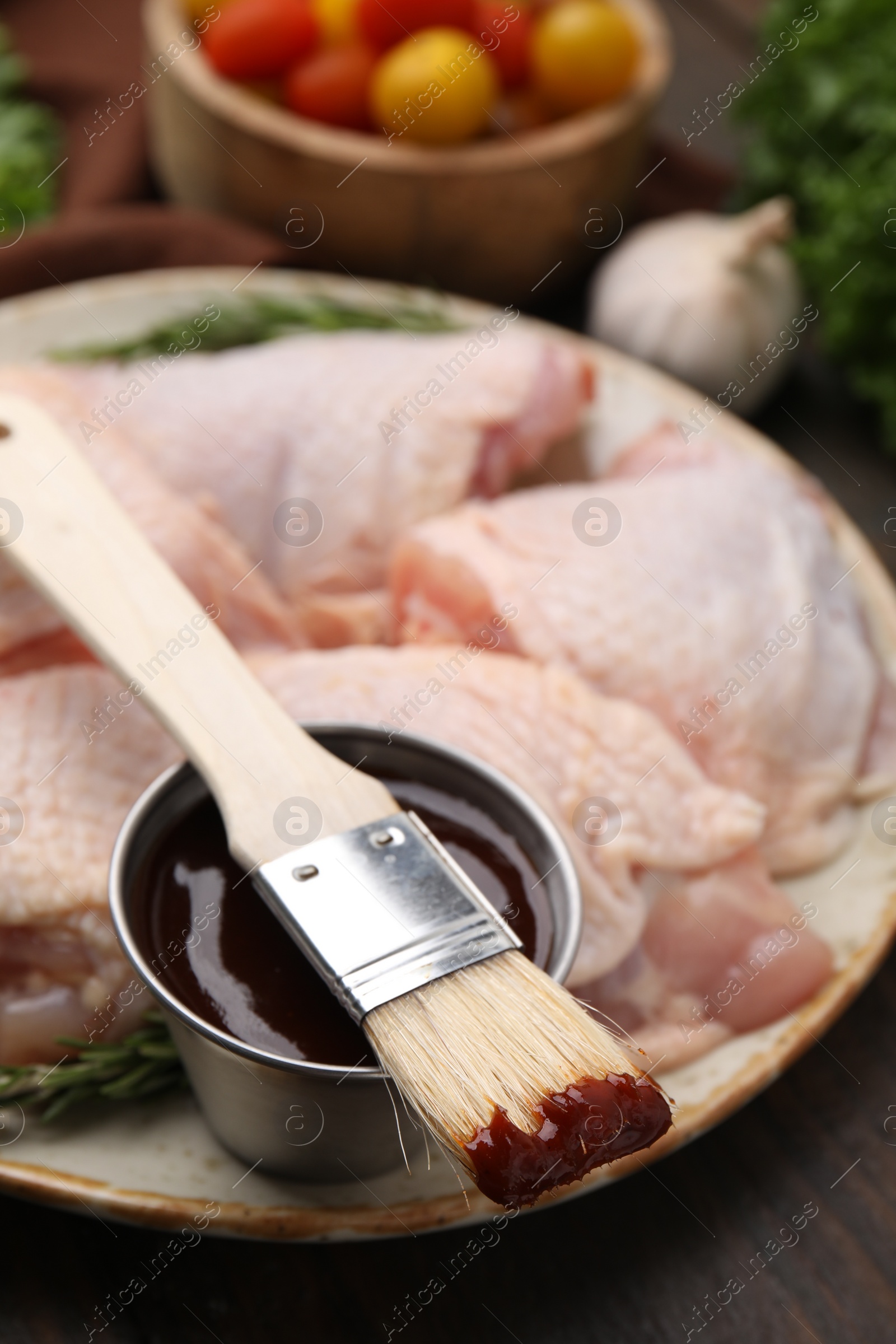 Photo of Plate with fresh marinade, raw chicken and basting brush on wooden table, closeup