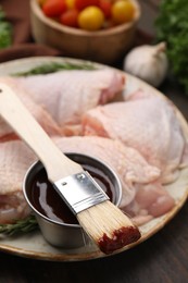 Photo of Plate with fresh marinade, raw chicken and basting brush on wooden table, closeup
