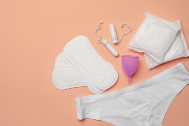 Photo of Flat lay composition with underwear, menstrual cup and other feminine hygiene products on pale orange background, space for text