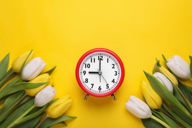 Red alarm clock and beautiful tulips on yellow background, flat lay. Spring time