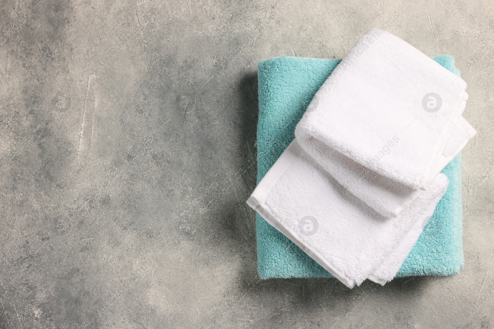 Photo of Soft folded terry towels on light gray textured background, top view. Space for text