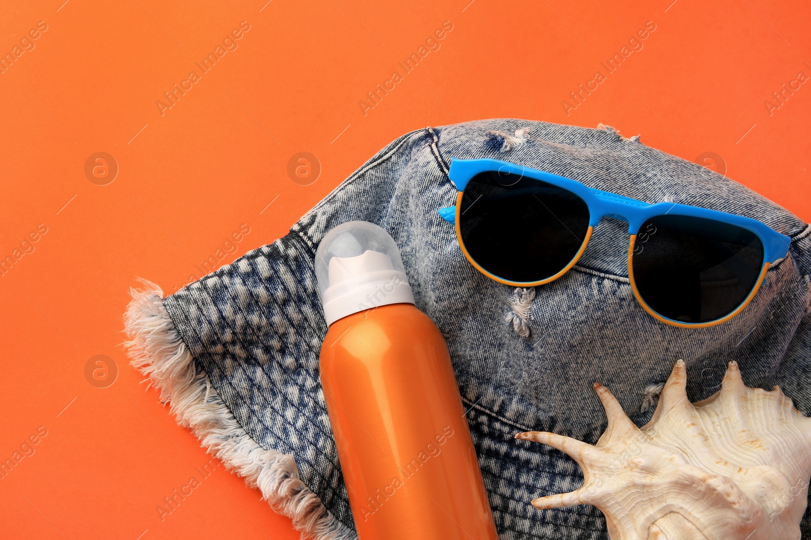 Photo of Bottle of sunscreen, seashell and beach accessories on coral background, flat lay