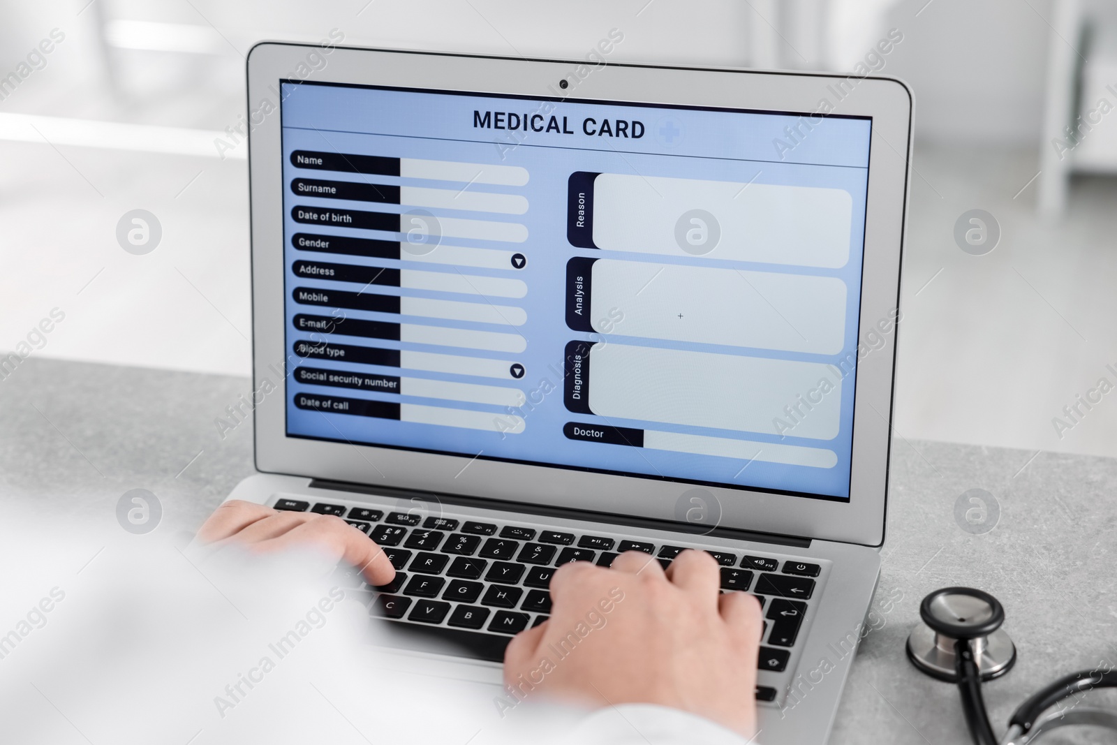 Photo of Doctor using laptop to fill out patient's medical card at table in clinic, closeup