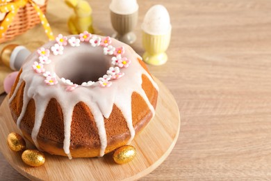 Photo of Delicious Easter cake decorated with sprinkles near eggs on wooden table, closeup. Space for text