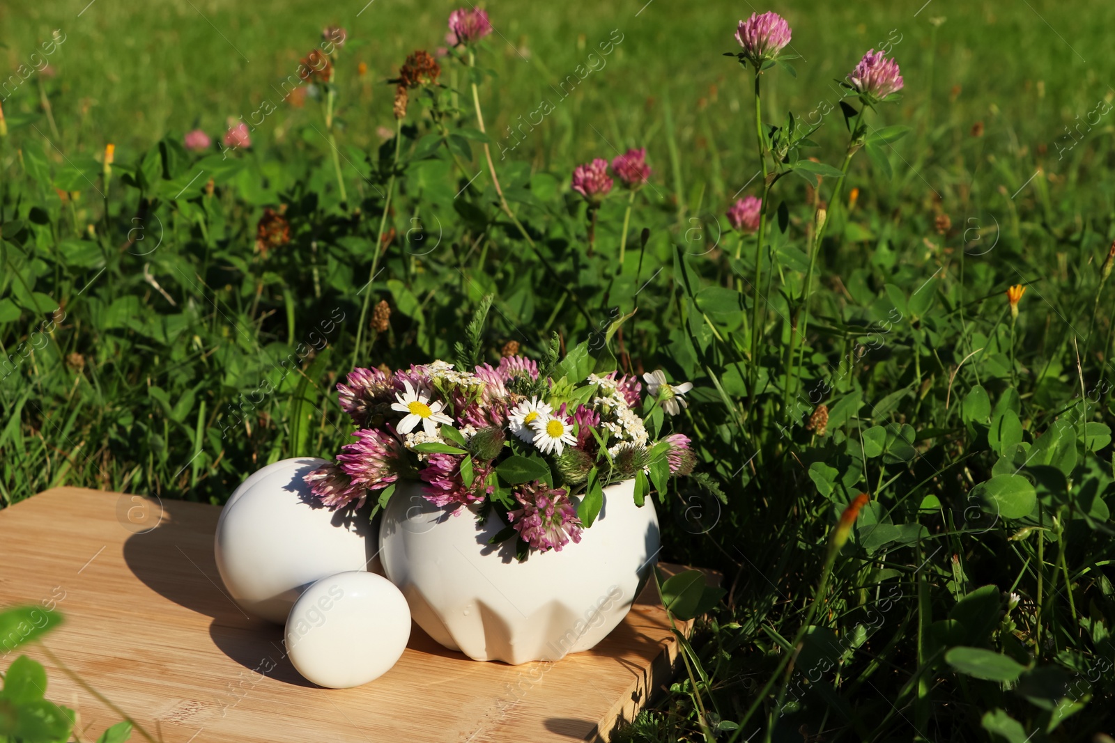 Photo of Ceramic mortar with pestle, different wildflowers and herbs on wooden board in meadow. Space for text
