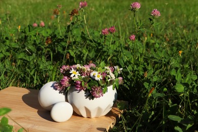Photo of Ceramic mortar with pestle, different wildflowers and herbs on wooden board in meadow. Space for text