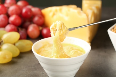 Photo of Piece of bread over bowl with delicious cheese fondue on gray table