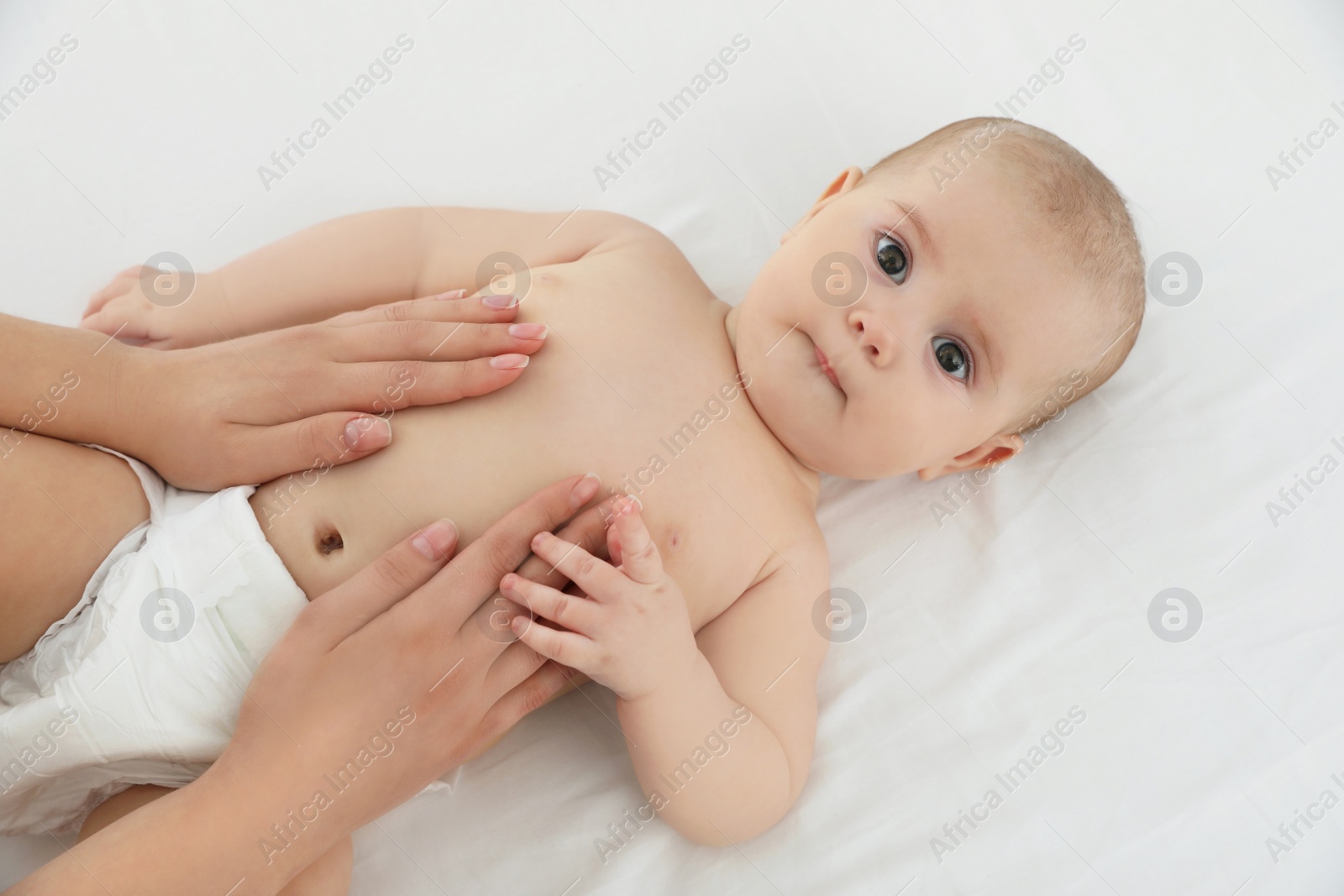 Photo of Mother and her cute child on white bed, above view. Baby massage and exercises