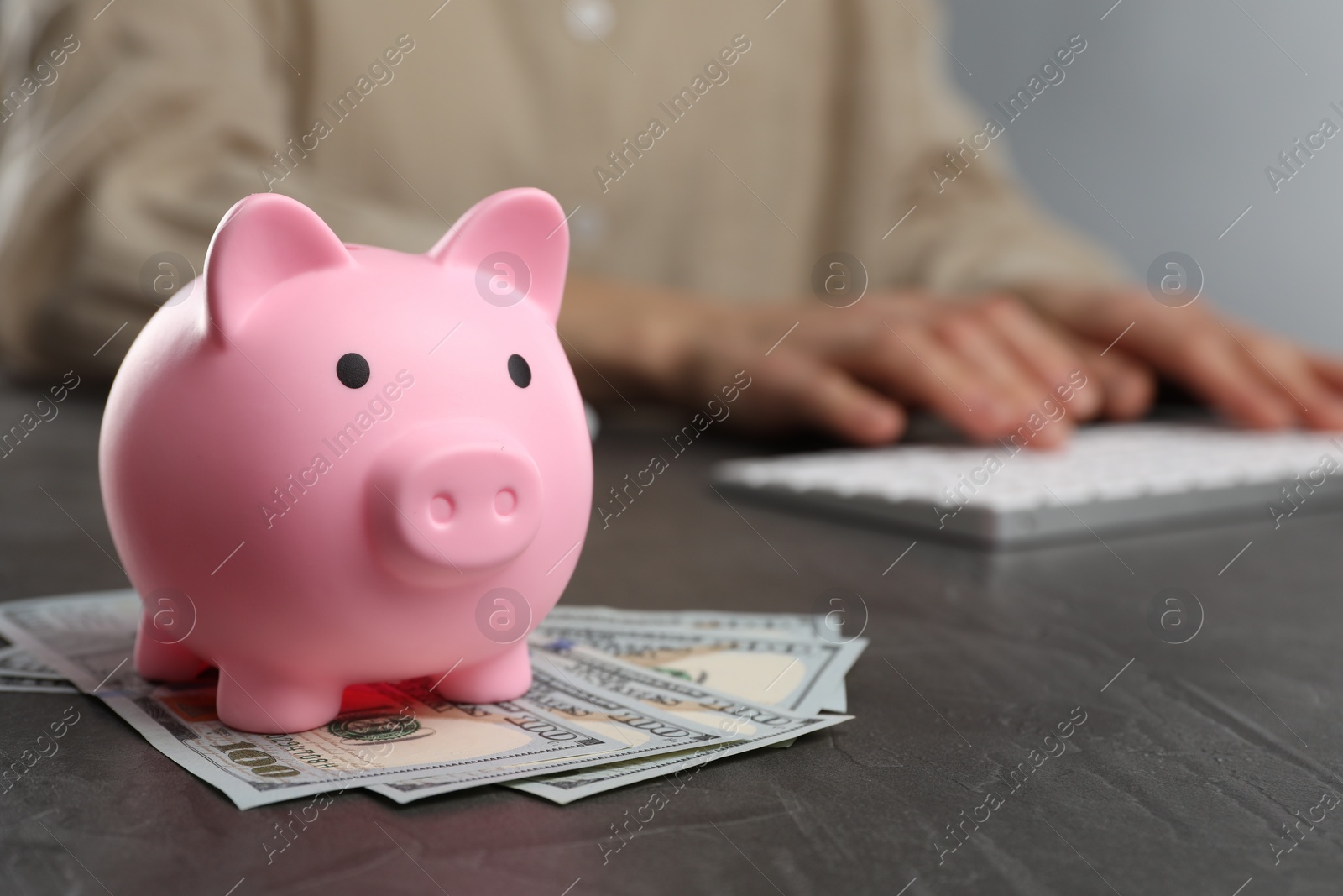 Photo of Woman at black table, focus on pink piggy bank and banknotes. Space for text