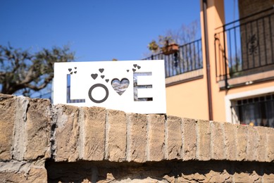 Photo of Board with word LOVE on brick fence outdoors