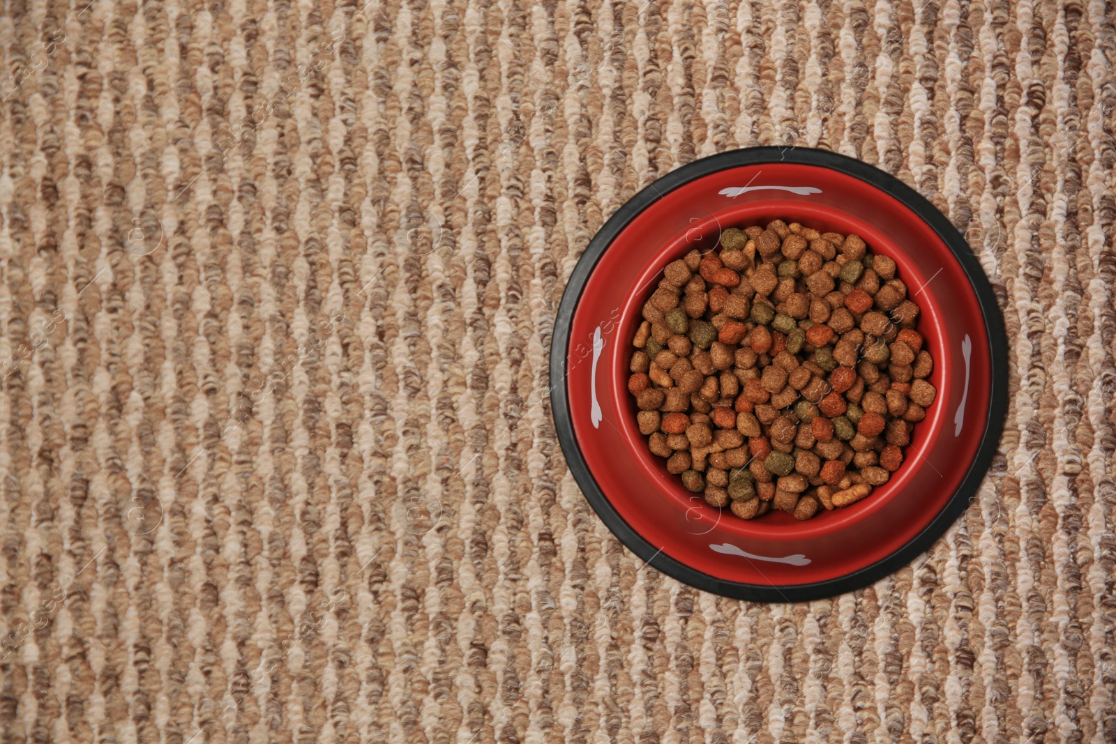 Photo of Dry dog food in feeding bowl on soft carpet, top view. Space for text